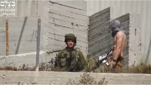Un colon israélien masqué en pantalon militaire tire sur des Palestiniens avec un soldat à côté de lui, ‘Urif